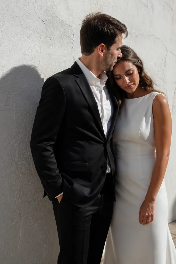 Couple stands against a white wall with side lighting creating strong shadows