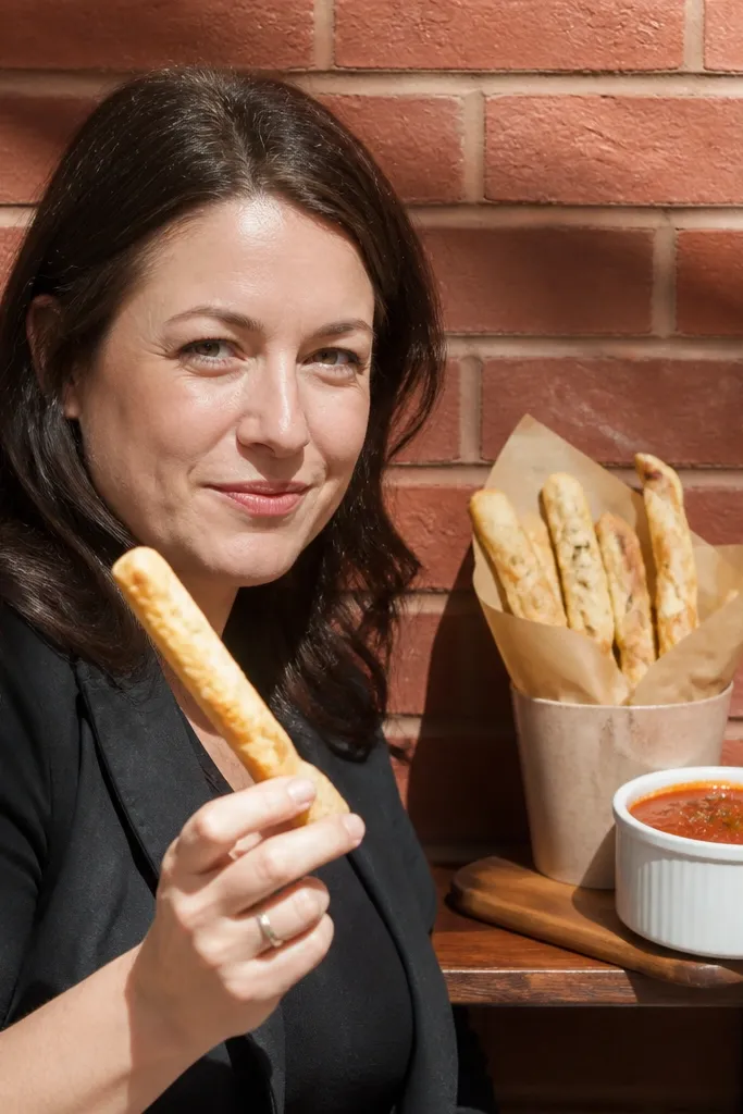 Breadsticks and marinara cups on a table against a brick wall
